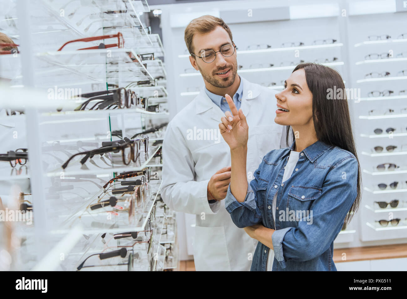 Donna sorridente rivolta dal dito a ripiani con occhiali a maschio all'ottico optometrista in optica Foto Stock