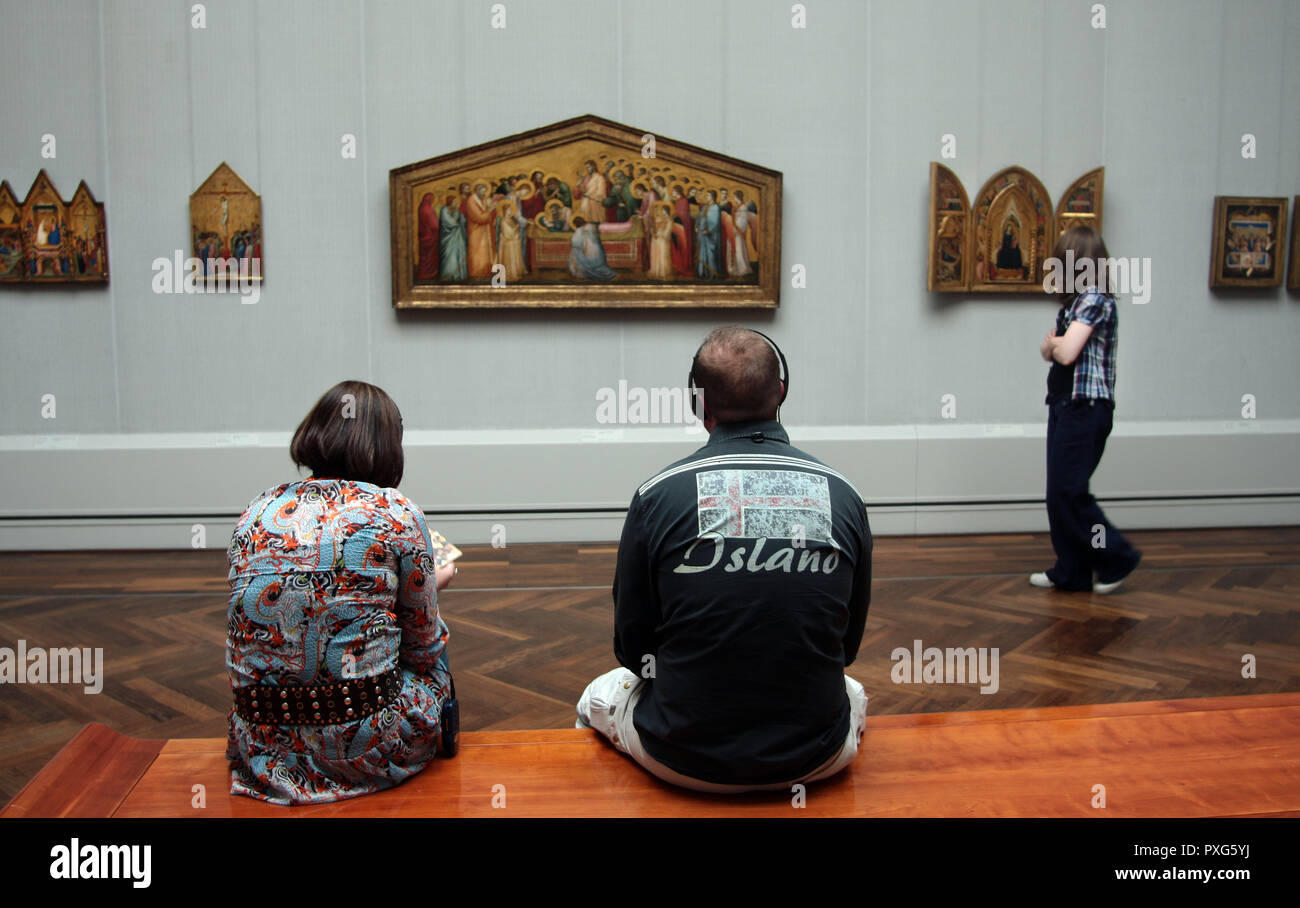 Tre persone sono in una galleria d'arte guardando l'arte sulle pareti. Due sono seduti e uno indossa le cuffie e la terza persona in piedi separatamente sul suo proprio in questa galleria a Berlino. Foto Stock