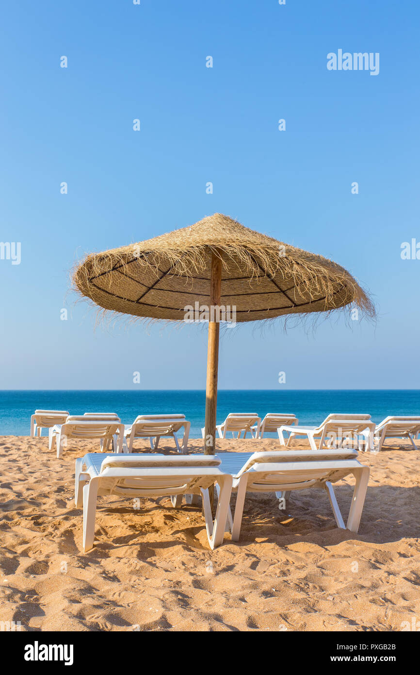 Uno di vimini ombrellone in spiaggia con lettini al mare blu Foto Stock