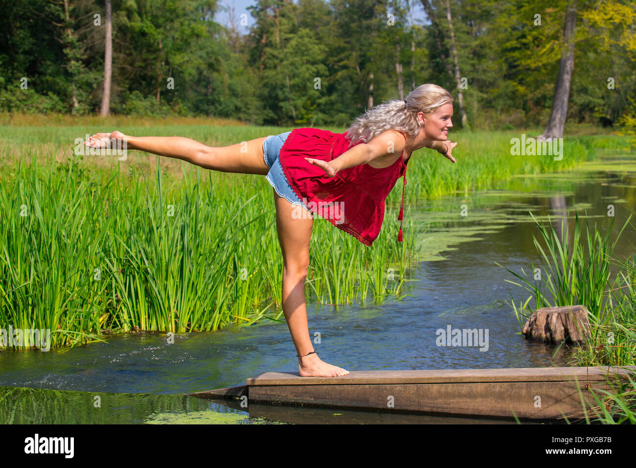 Giovane donna bionda in postura yoga su una gamba in natura Foto Stock