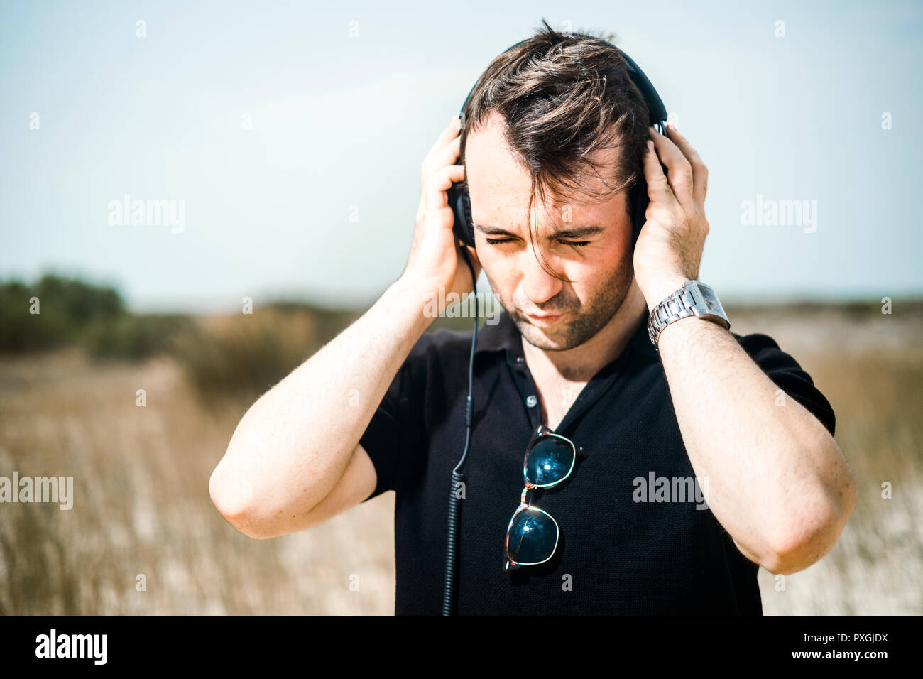 Giovane uomo attraente vestita di nero godendo di musica sul suo cuffie Foto Stock