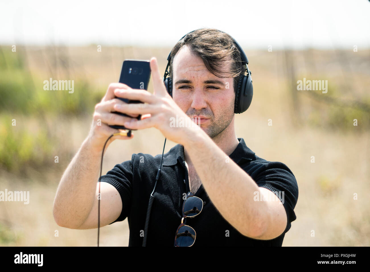 Moda giovane uomo ascolta la musica dal suo smartphone su le sue cuffie Foto Stock