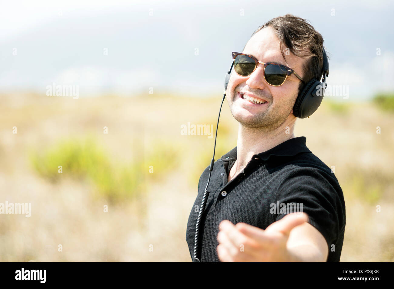 Giovane uomo attraente indossando occhiali da sole godendo di musica sul suo cuffie Foto Stock