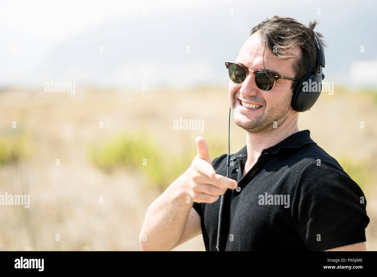 Giovane uomo attraente indossando occhiali da sole e le cuffie che punta verso la telecamera Foto Stock