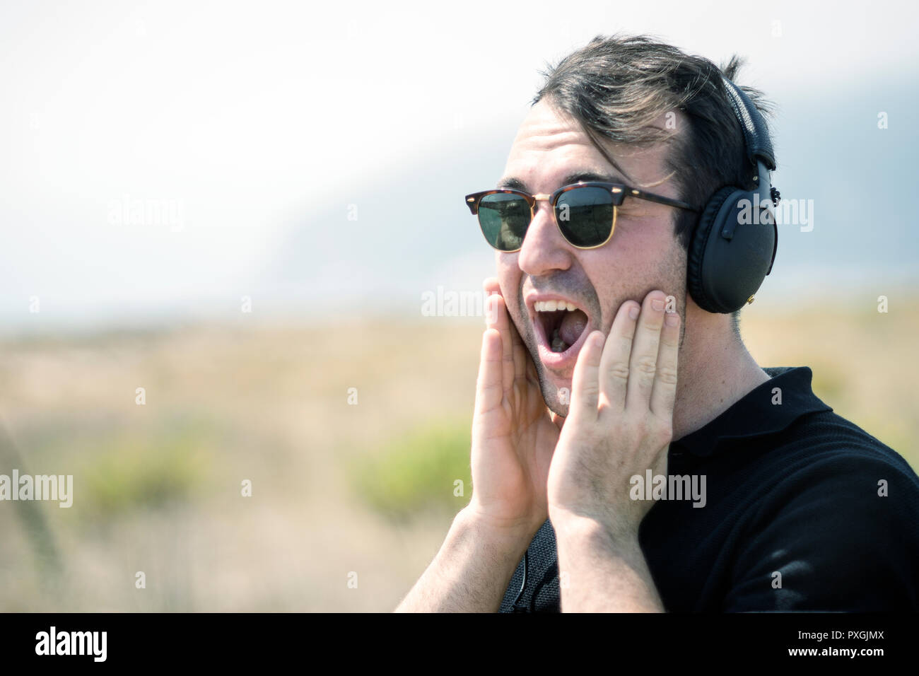 Sorpreso attraente uomo che indossa gli occhiali da sole e le cuffie durante la giornata di sole Foto Stock