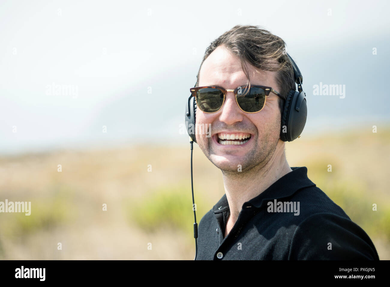 Giovane uomo attraente indossando occhiali da sole godendo di musica sul suo cuffie Foto Stock
