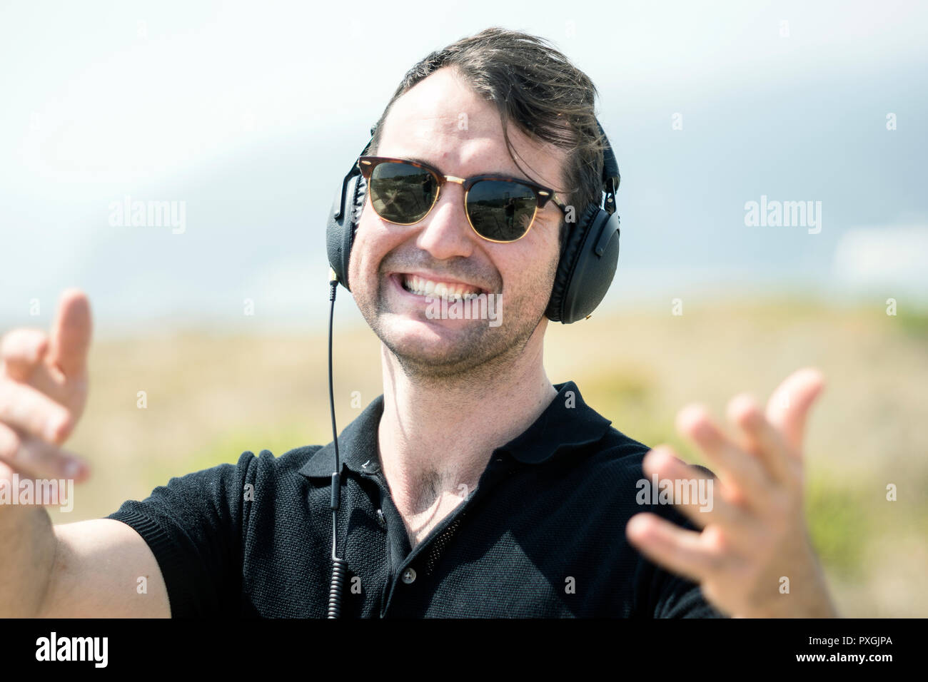 Felice, attraente uomo che indossa gli occhiali da sole godendo di musica sul suo cuffie Foto Stock