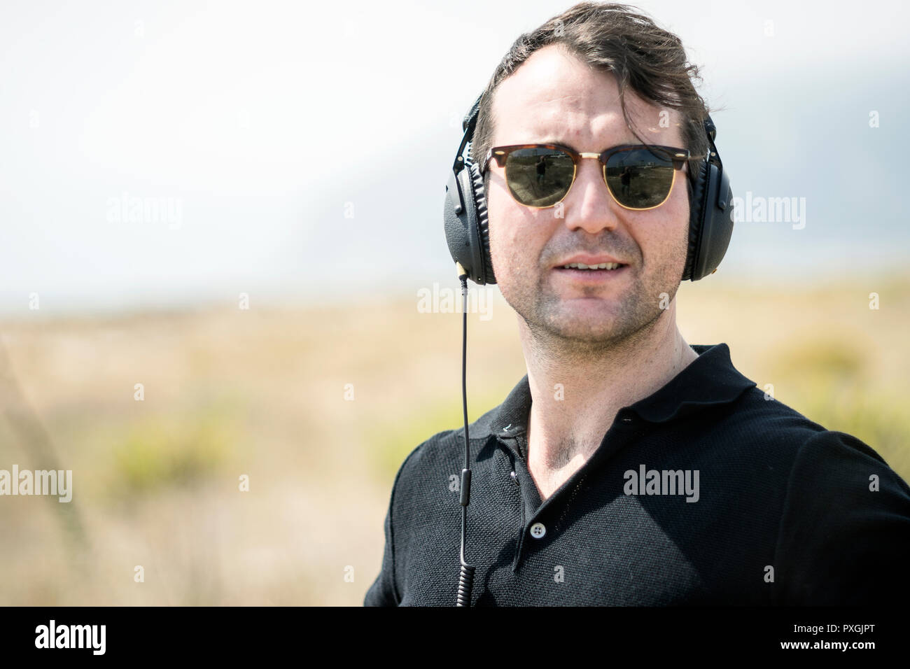 Giovane uomo attraente indossando occhiali da sole godendo di musica sul suo cuffie Foto Stock