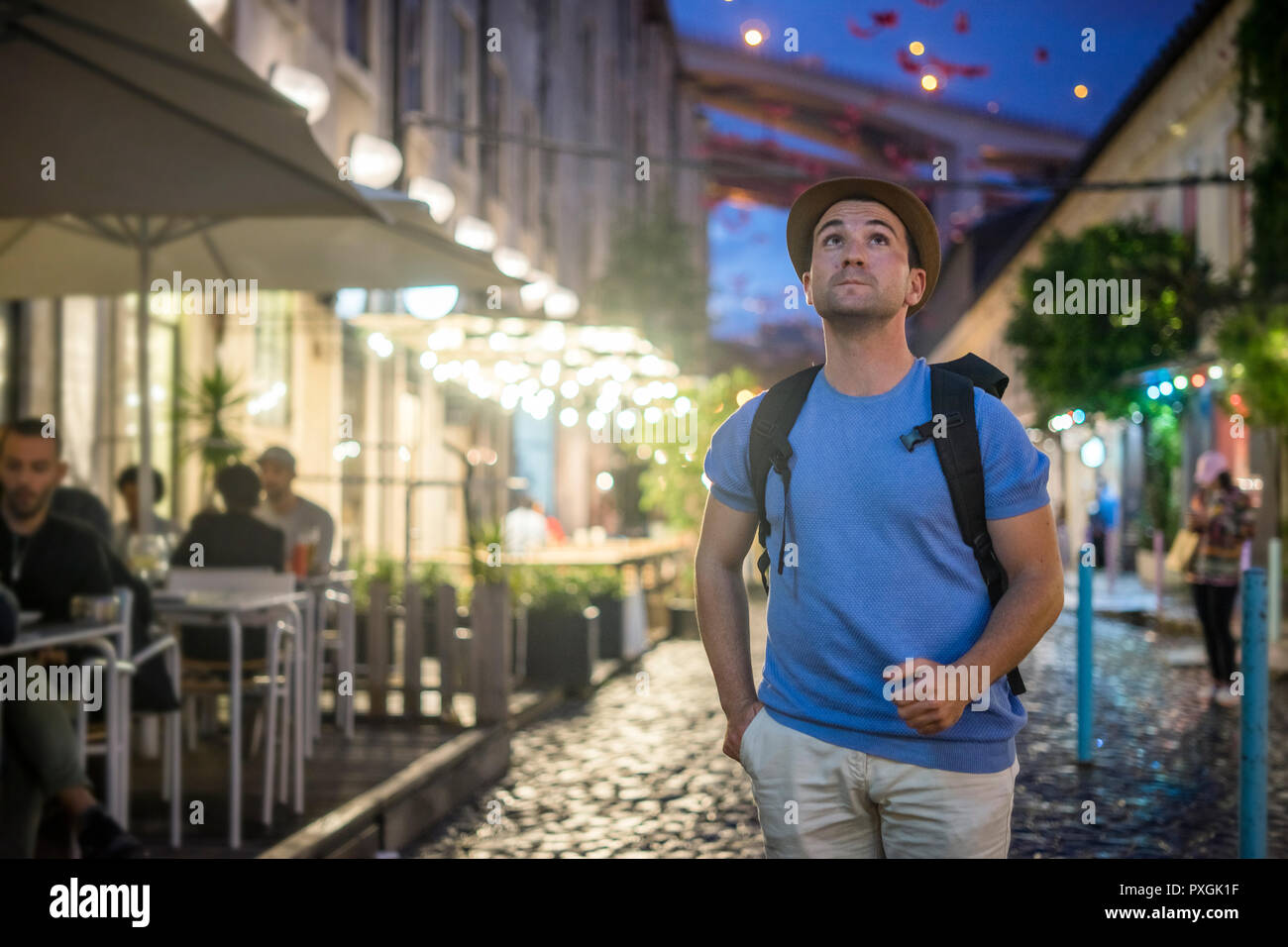 Giovane Uomo in camicia blu a piedi su strade vivaci e cercando fino alla sera Foto Stock