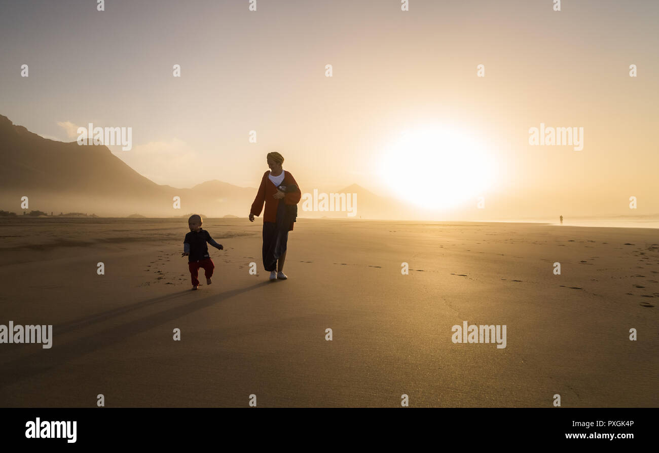 Silhouette della giovane madre con il suo bambino camminando sul sole di Cofete, Fuerteventura, Isole Canarie, Spagna. Foto Stock
