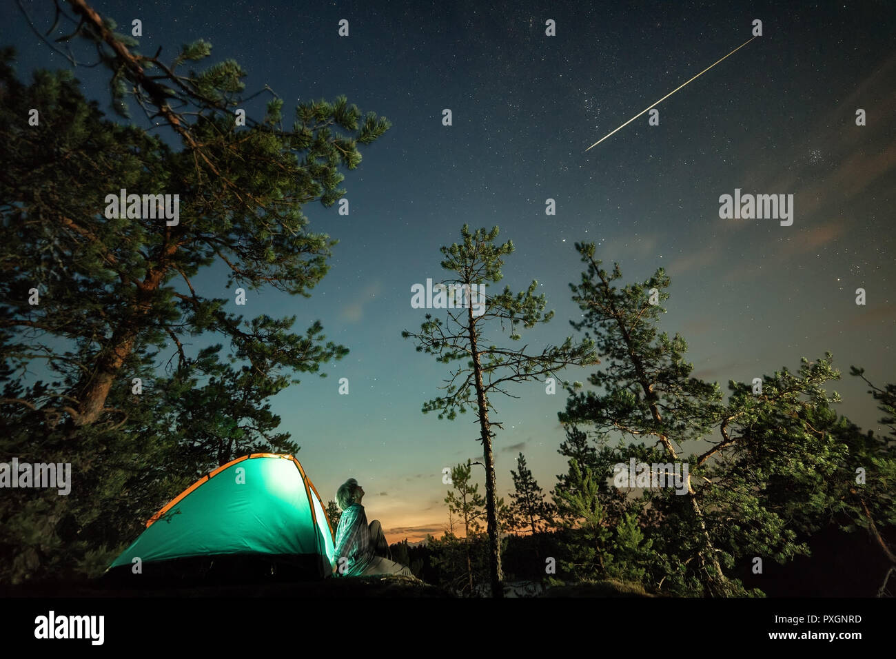 Uomo che guarda sulla vicina cielo stellato con stella cadente. Esterno notte scena. Una lunga esposizione, grana visibile Foto Stock