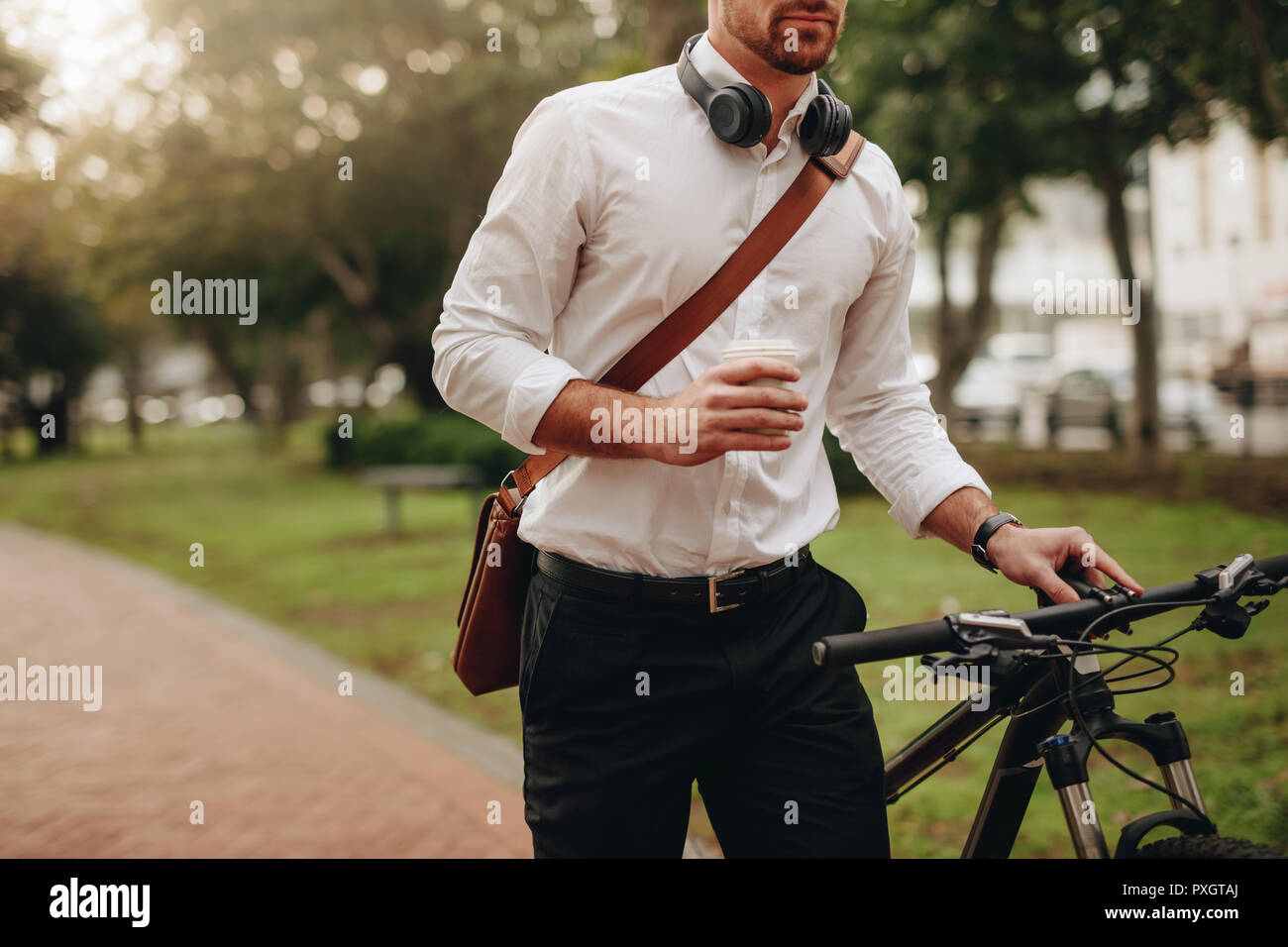 Imprenditore tenendo una tazza di caffè e a piedi per office prendendo la sua bicicletta lungo. L'uomo bere un caffè mentre si cammina a lavorare insieme con la sua moto. Foto Stock