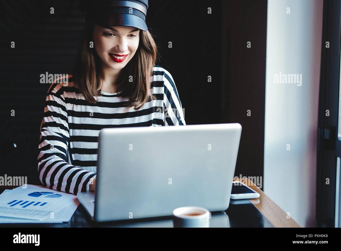 Concentrati sul lavoro. Fiducioso giovane donna in smart casual lavorando sul computer portatile mentre è seduto vicino alla finestra in ufficio creativo o cafe. Foto Stock