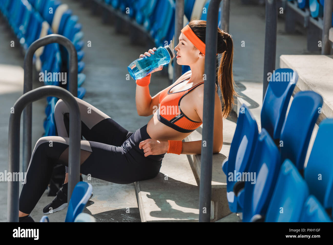 Vista laterale del stanco giovane donna acqua potabile su scale presso lo stadio sportivo Foto Stock