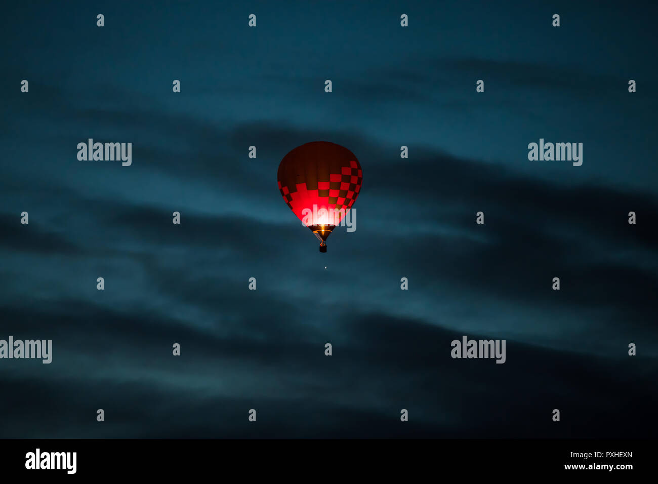 Coloratissima mongolfiera in rosa scuro e colori porpora incandescente in un blu scuro la mattina presto il cielo con le nuvole drammatico Foto Stock