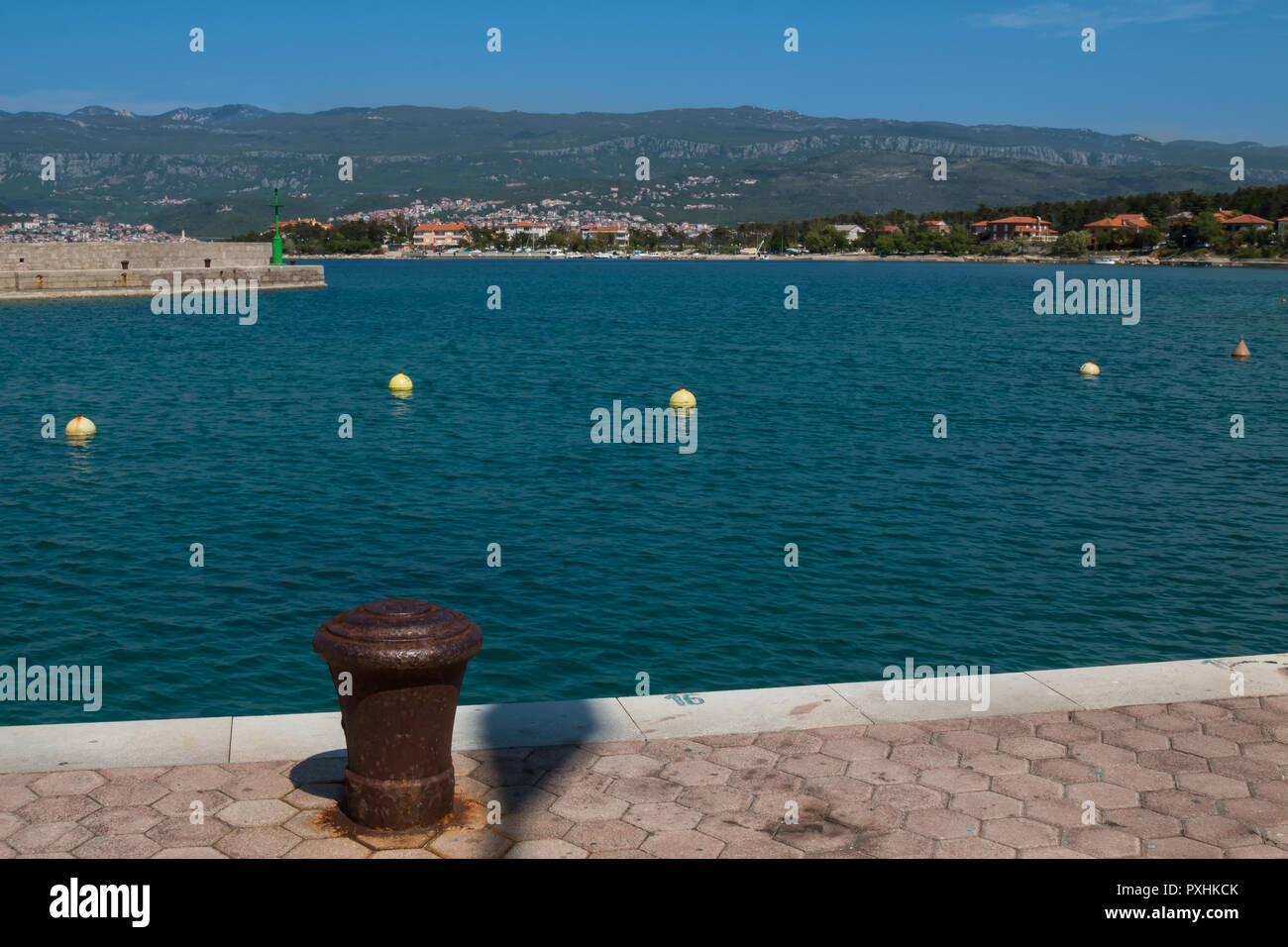 Rive del mare adriatico bay, con un ancoraggio arrugginito per legare la barca, al momento vuoto. Onde di un mare azzurro, montagne e villaggi in backgroun Foto Stock