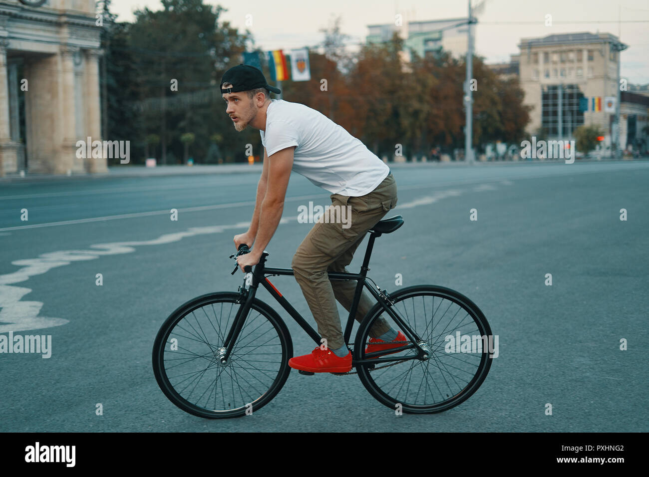 Vista laterale giovane uomo moderno ciclismo su un classico moto sulla strada della città. Copia dello spazio. Attivo e stile di vita ecologico concetto Foto Stock