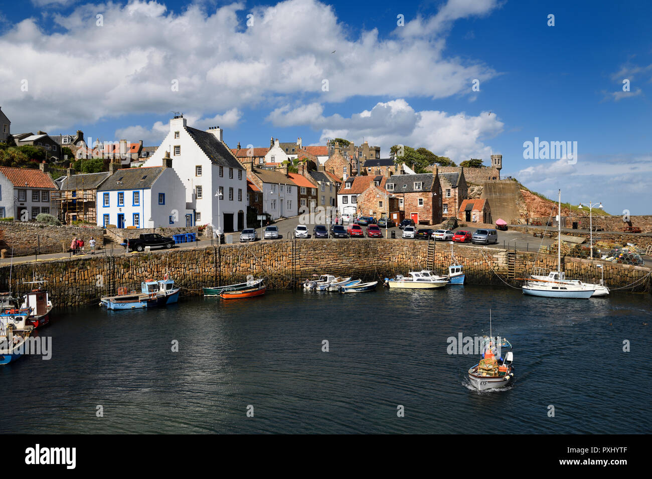 Pescatore in barca lasciando Crail Harbour con pilastri di pietra e Crail torretta della casa che si affaccia sul Mare del Nord Scozia UK Foto Stock