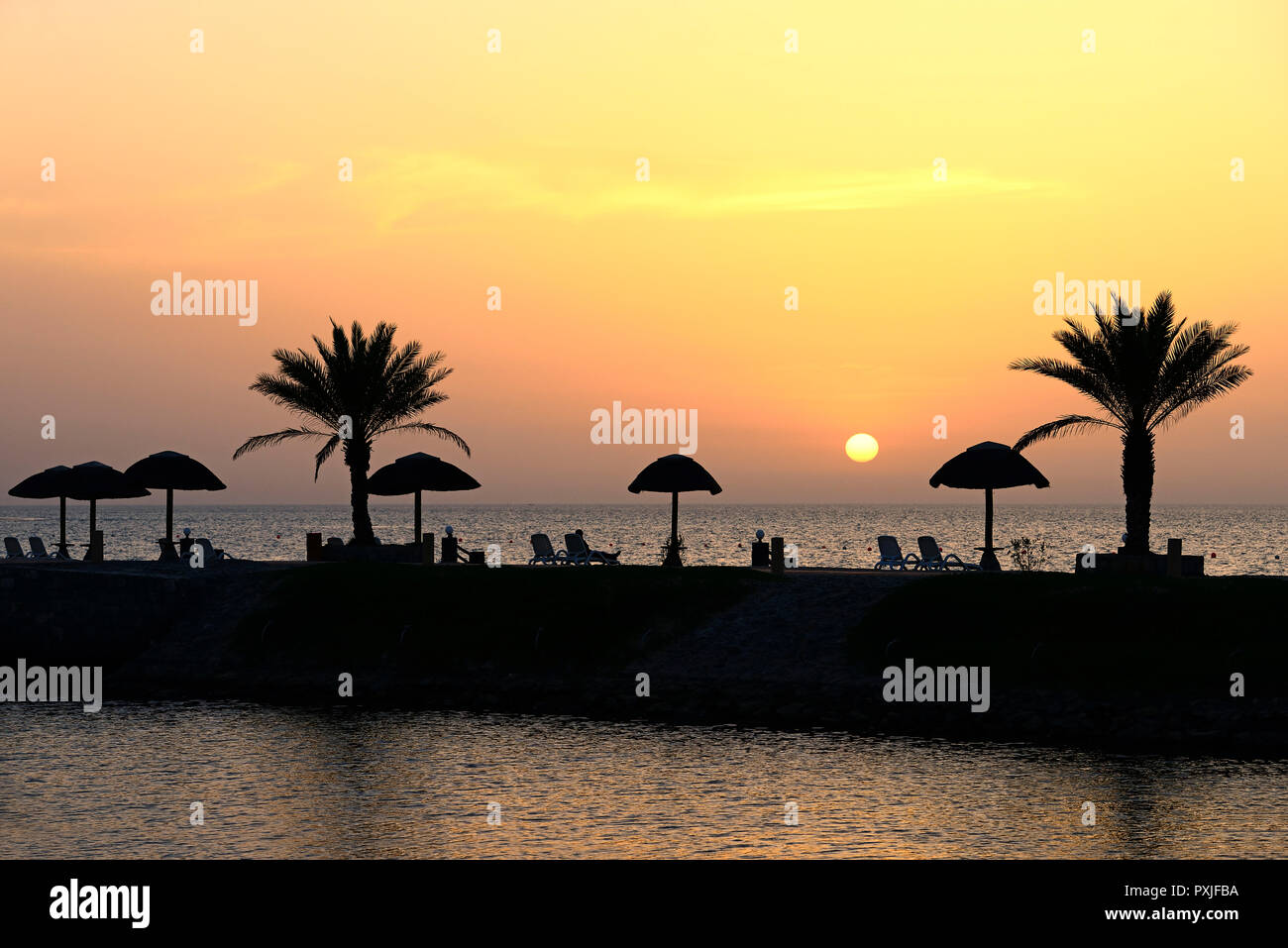 Tramonto con acqua dalla riflessione di palme e ombrelloni, Hotel Cove Rotana, Ras al Khaimah Emirati Arabi Uniti Foto Stock