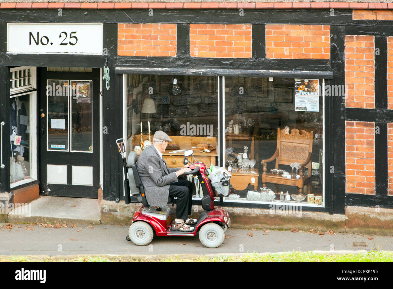 Anziani vecchio uomo persona su una mobilità scooter smesso di guardare nella vetrina di un negozio di antiquariato Foto Stock