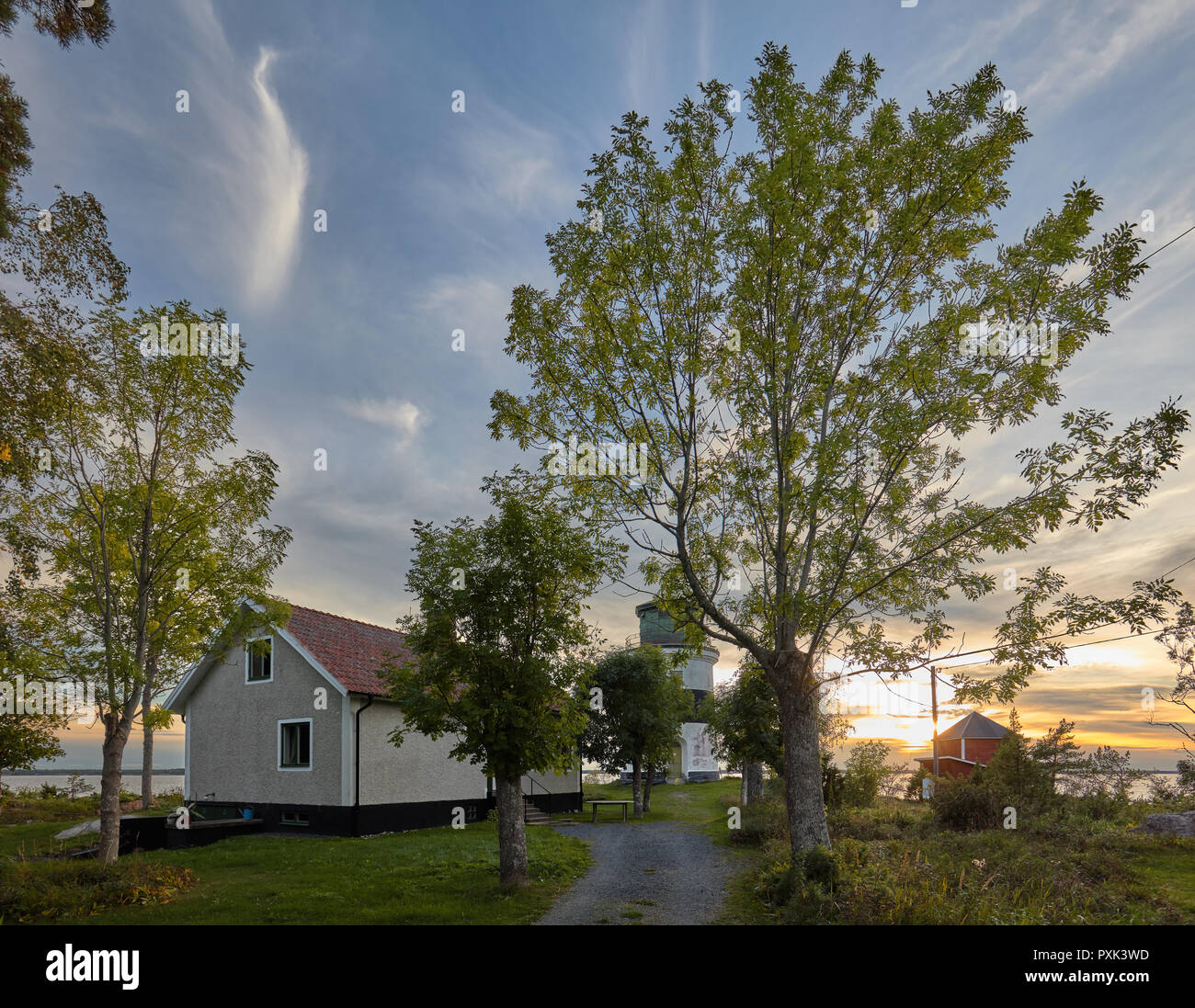 Vista in un faro, house e un albero contro un bel tramonto Cielo di sera con soffici nuvole in Gräsö, Svezia Foto Stock