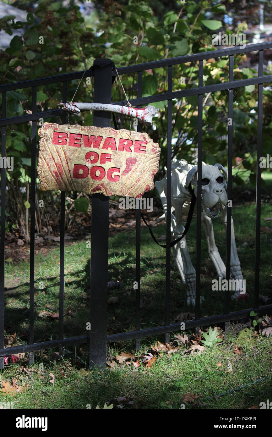Super creepy, inquietante e lugubre Decorazione Halloween 'attenzione.non firmi appeso accanto a uno scheletro di cane e visualizzati su un prato anteriore. Foto Stock