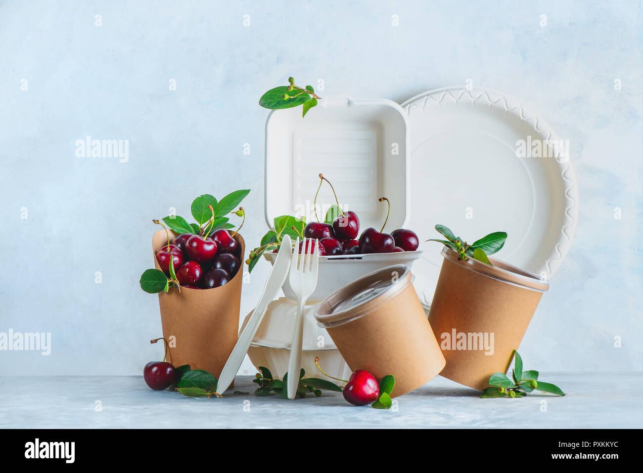Catering monouso, tazze, piatti e contenitori con ciliegie. Eco-friendly packaging alimentare su uno sfondo grigio neutro con copia spazio. Preservare Foto Stock