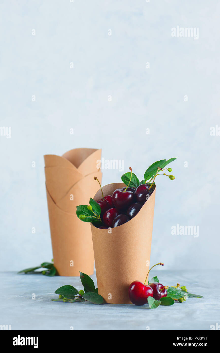 Carta Craft eco-friendly packaging alimentare con ciliegie. Tazze monouso su uno sfondo grigio neutro con copia spazio. Conservare la natura e il riciclaggio c Foto Stock