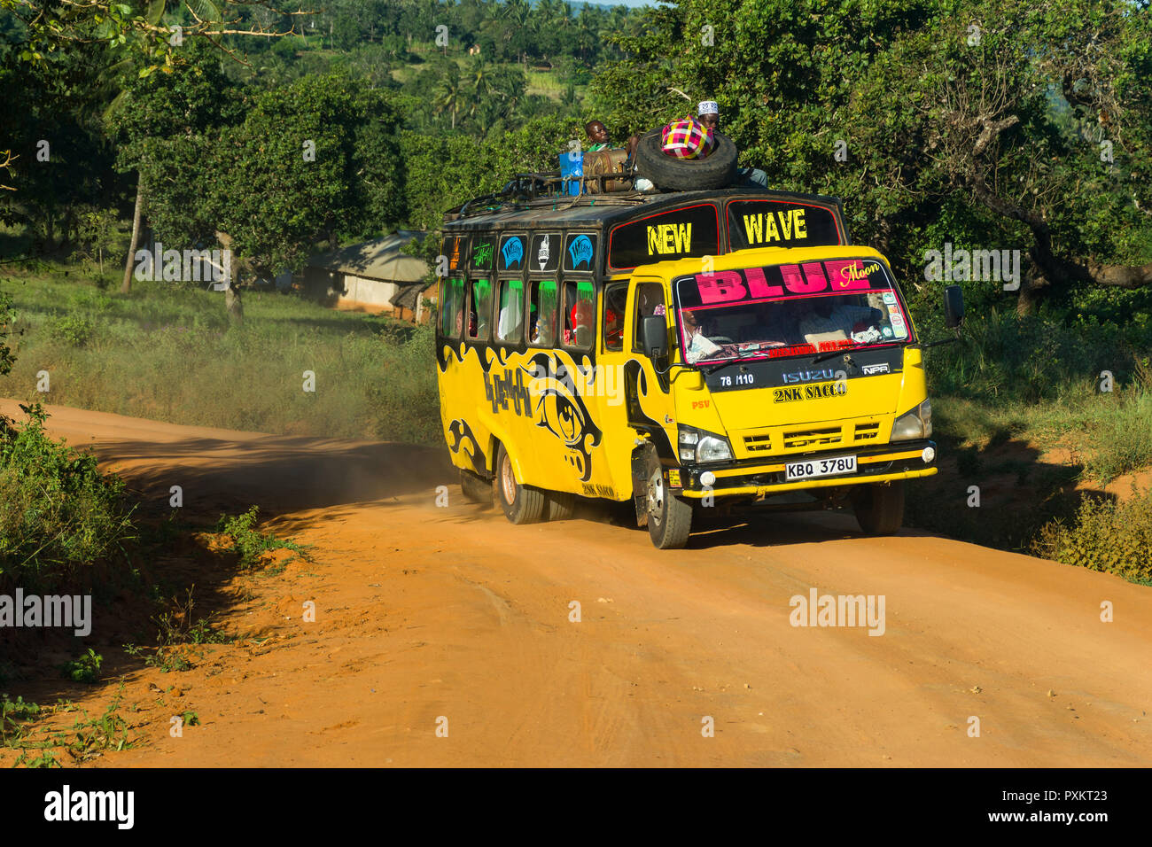 Un colorato autobus gialli viaggia lungo una strada polverosa nelle zone rurali del Kenia Foto Stock