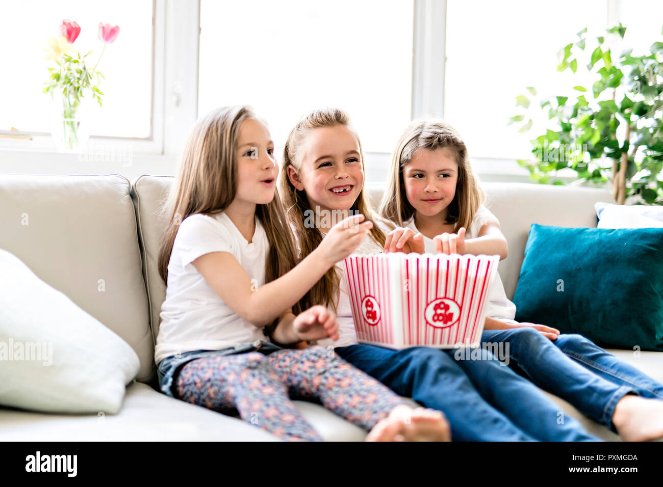 Tre piccolo felice girls watching commedia film sul televisore e mangiare popcorn a casa Foto Stock