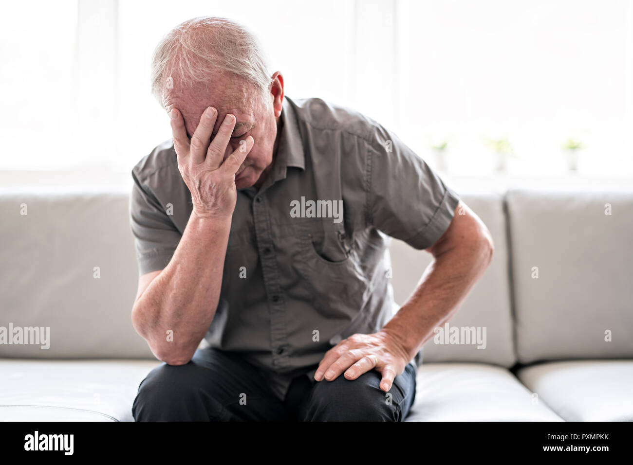 Senior uomo pensare e seduto sul divano di casa come triste Foto Stock