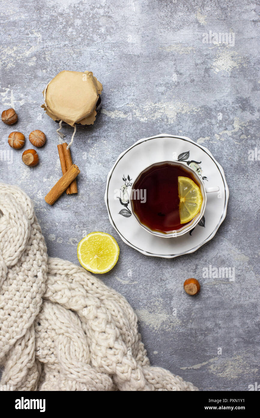 Ancora in vita e concetto di composizione. Tazza di tè nero e limone e piattino, limone, nocciola, bastoncini di cannella e sciarpa lavorata a maglia vicino, un backg grigio Foto Stock