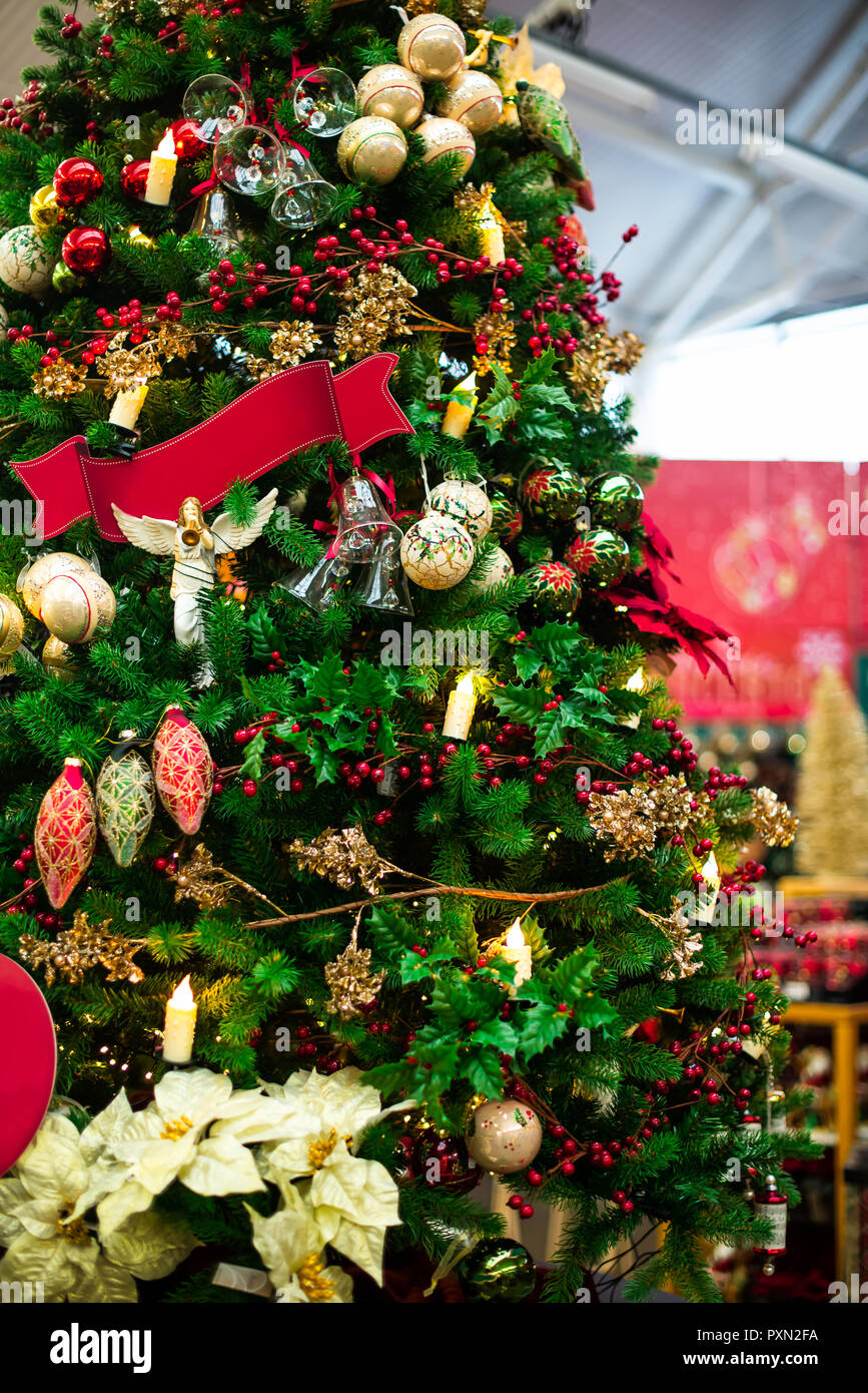 Albero di Natale decorato con rosso e decorazioni dorate, le luci sul mercato sfocata sullo sfondo. Scheda verticale. Morbida messa a fuoco selettiva, spazio di copia Foto Stock