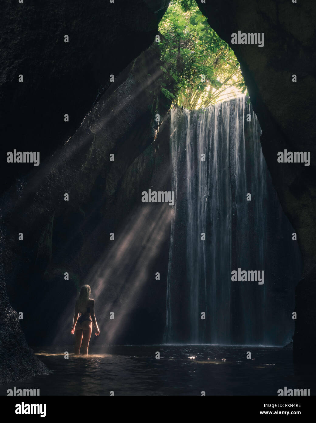 Una donna in piedi nel fiume di fronte a cascata, irraggiata dal raggio di luce Foto Stock