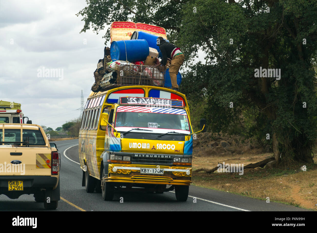 Un uomo di vincolare i bagagli sul tetto di un bus in movimento mentre si muove lungo una strada, Kenya Foto Stock