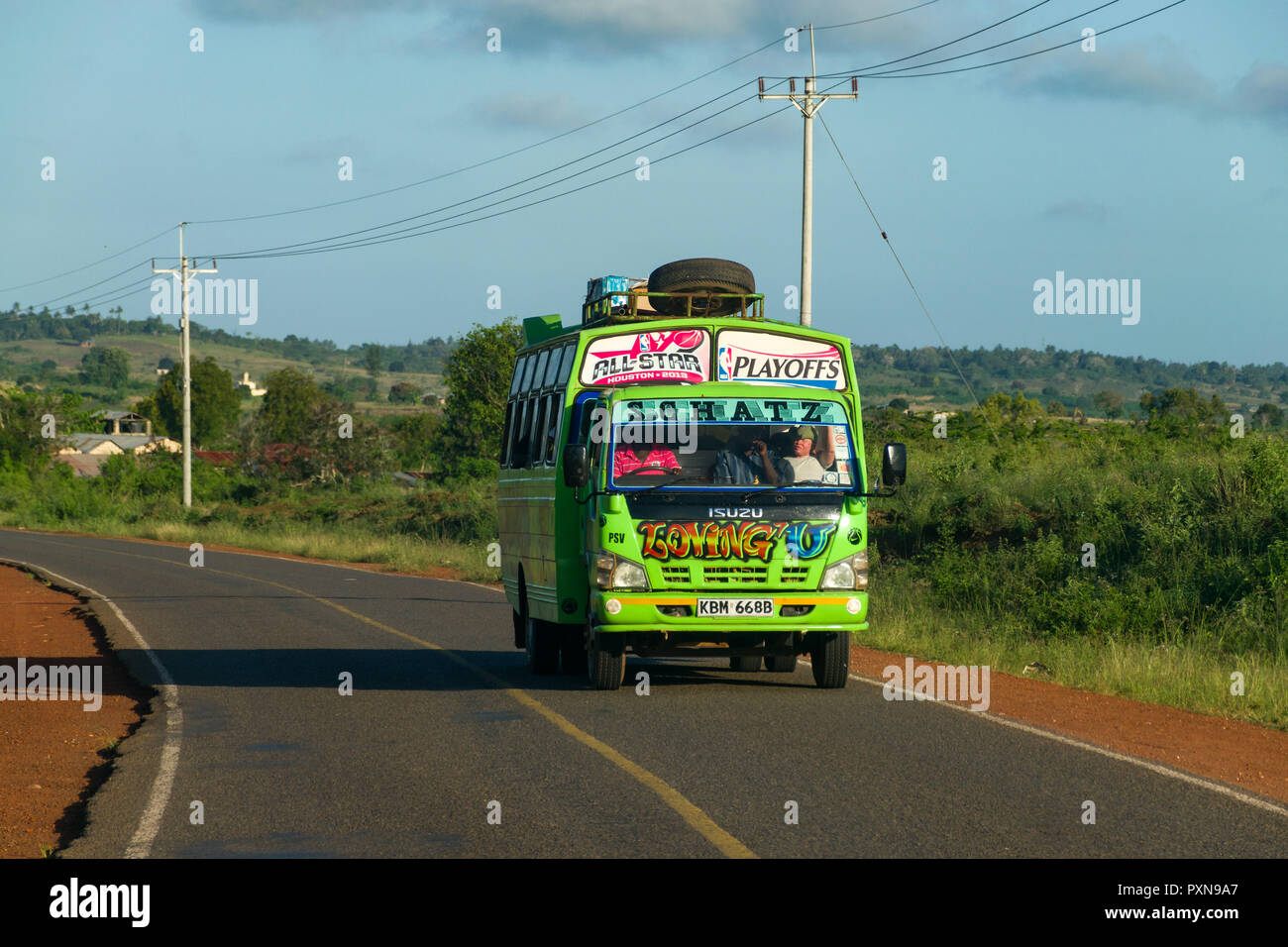 Un colorato autobus verde viaggia lungo una strada asfaltata nelle zone rurali del Kenia Foto Stock