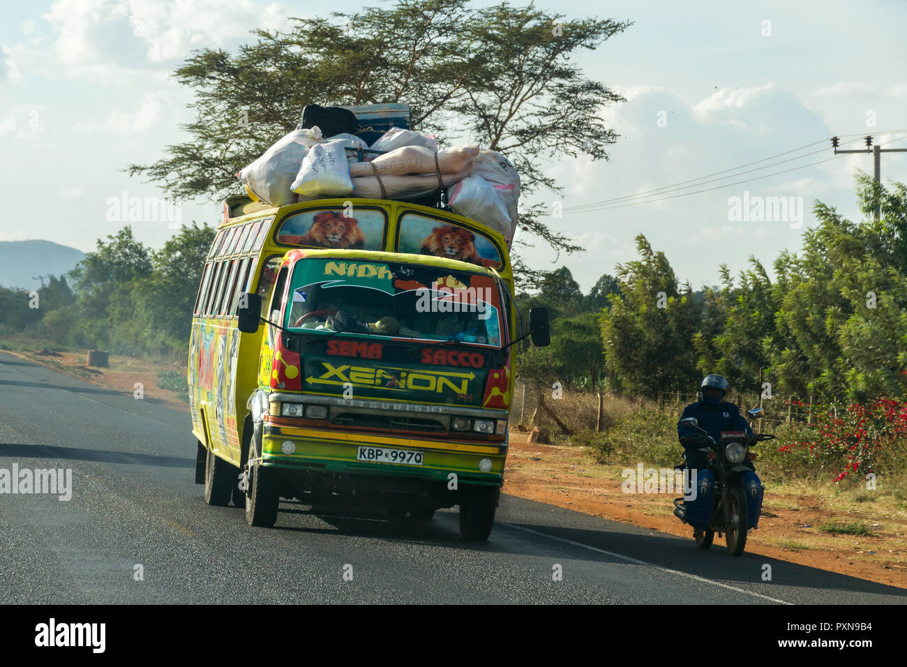 Un colorito autobus rigidi passato un motociclista sulla strada di Mombasa, in Kenya Foto Stock