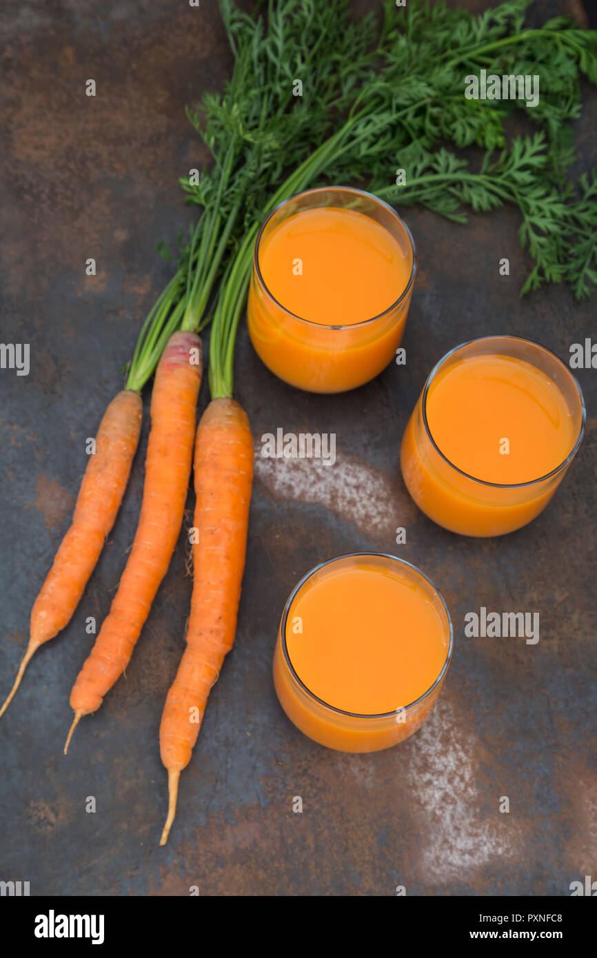 Tre Bicchieri di fresco succo di carota e tre carote Foto Stock