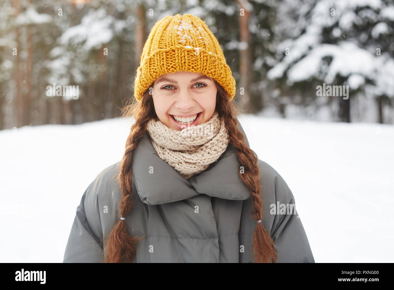 Allegro eccitato attraente ragazza dello studente in berretto lavorato a maglia e sciarpa a ridere mentre guardano la telecamera, lei passeggiate nella foresta di inverno Foto Stock
