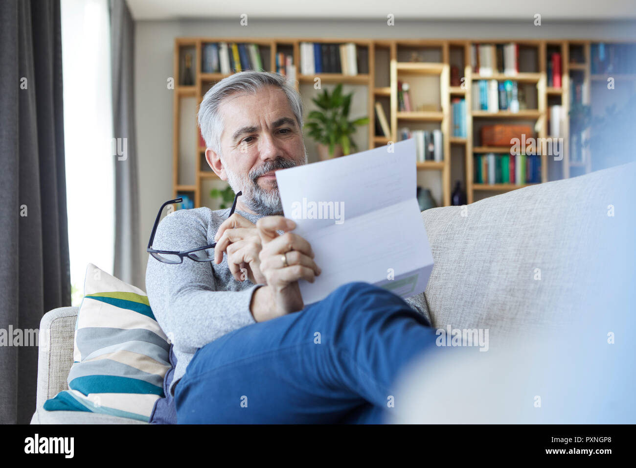 Uomo maturo seduto sul divano di casa lettura la lettera Foto Stock
