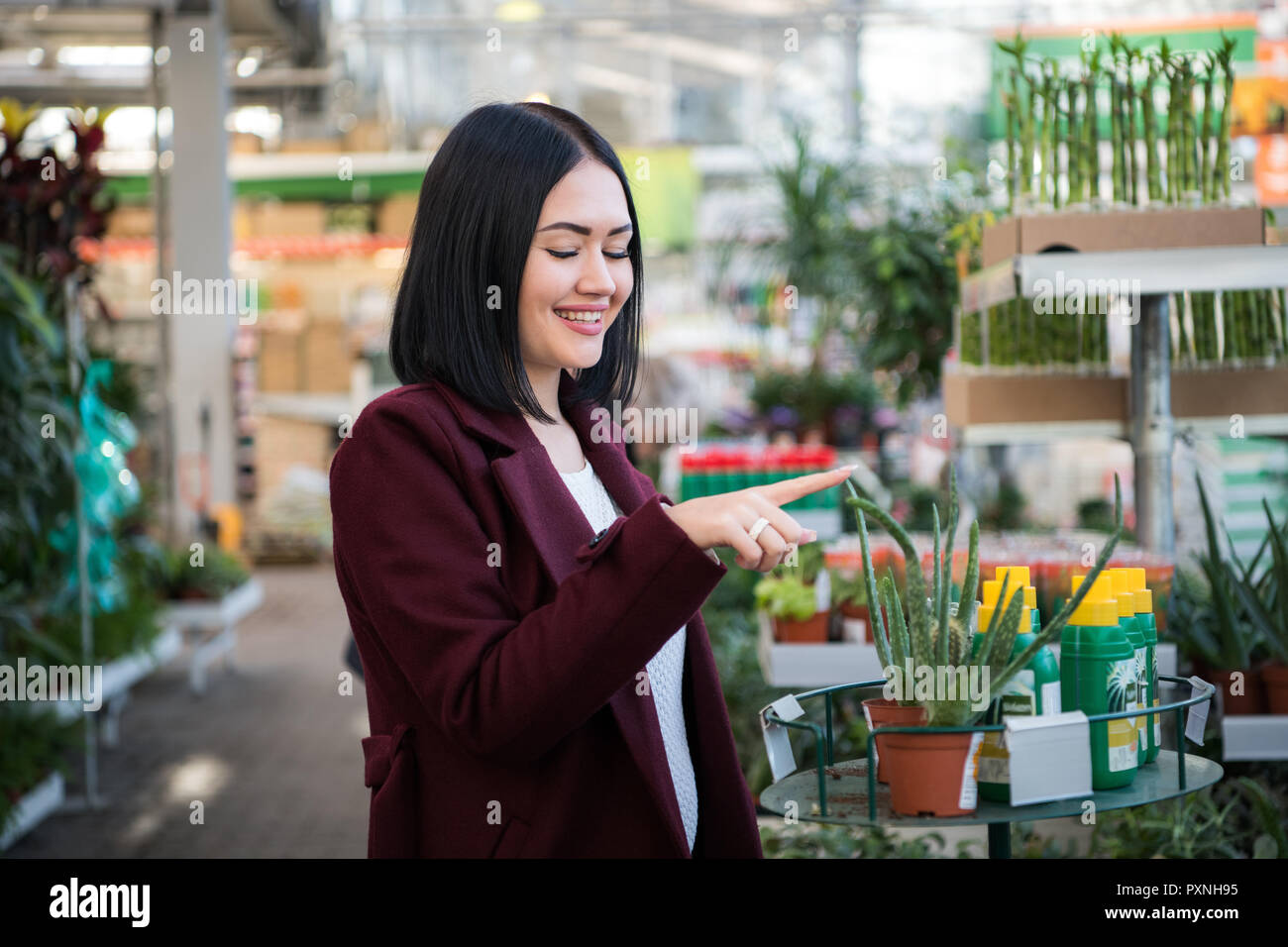 Giardiniere donna con carrello scelta di piante in un giardino centro Foto Stock