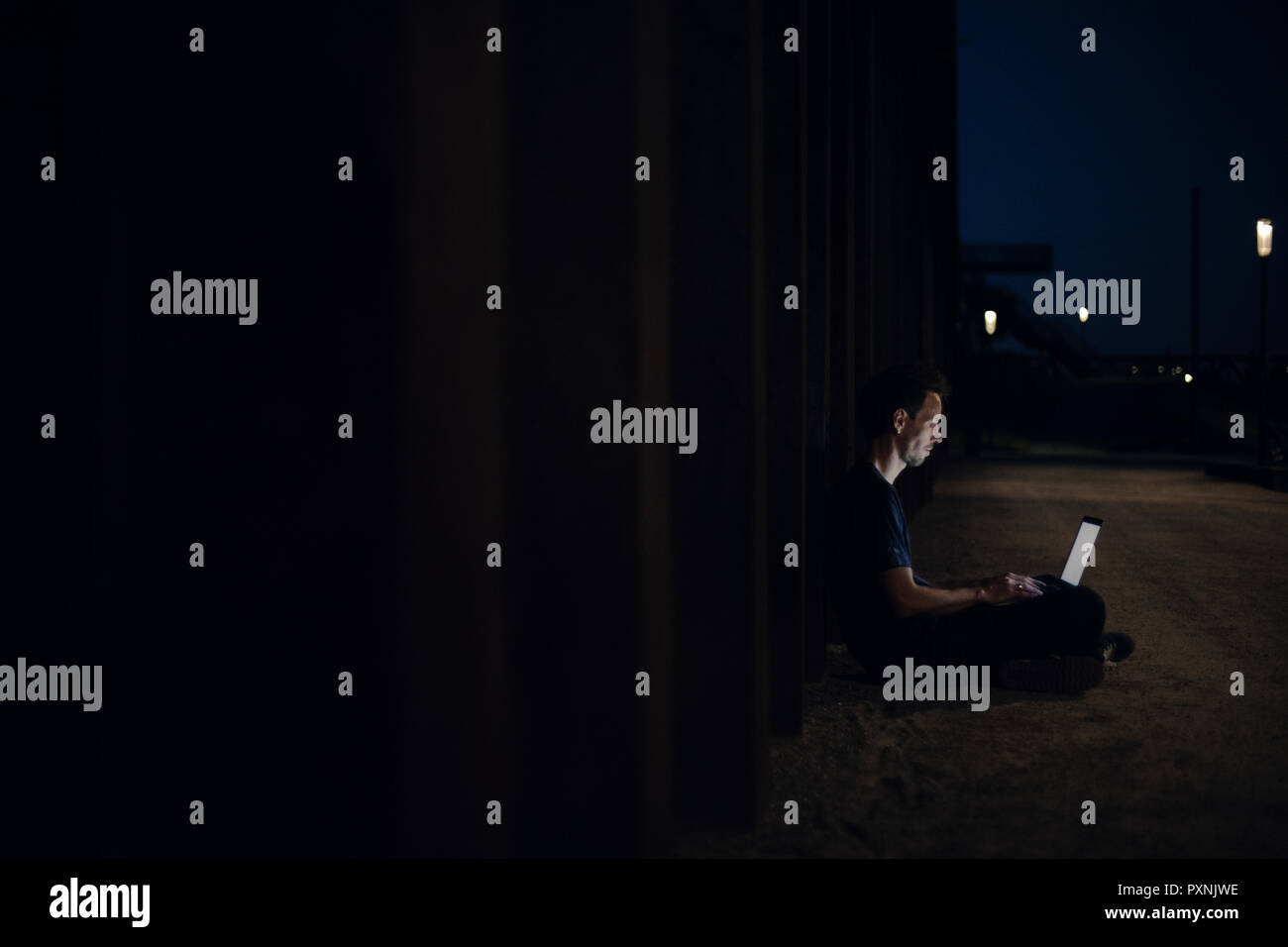 Metà uomo adulto seduto a gambe incrociate sulla terra, utilizzando computer portatile durante la notte Foto Stock