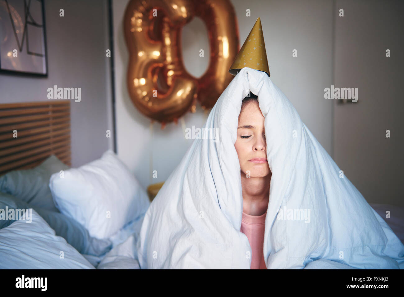 Triste donna festeggia il suo compleanno, seduta sul letto sotto coperta Foto Stock