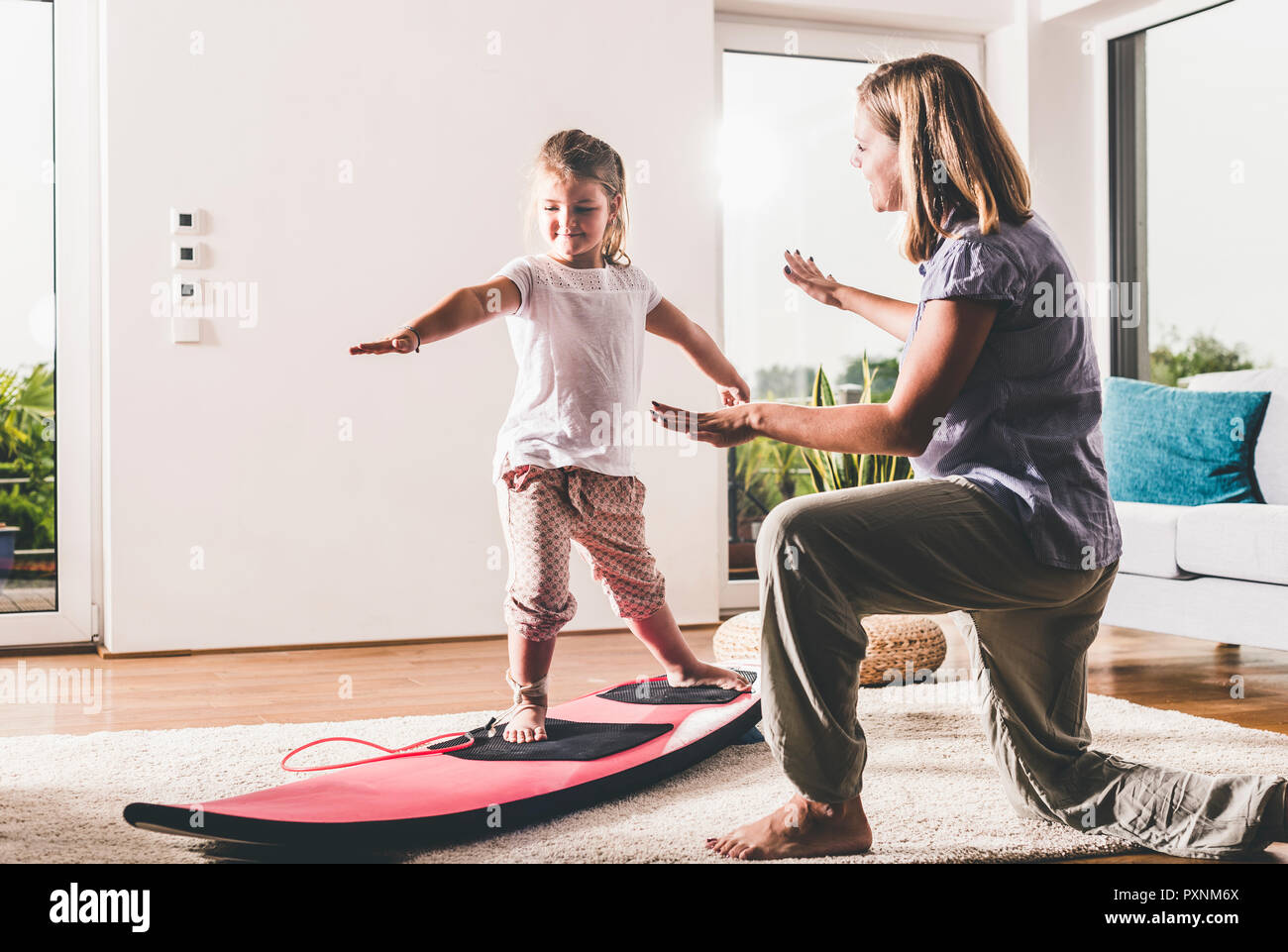 Madre e figlia esercitando con la tavola da surf in salotto Foto Stock