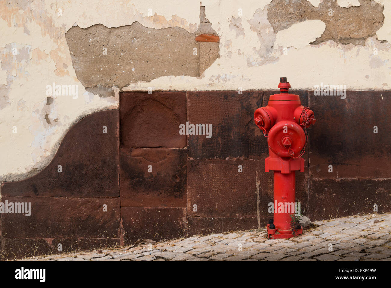 Il marciapiede lastricata da ciottoli. Idrante rosso. Sullo sfondo di un vecchio muro, parzialmente danneggiata. Città Silves, Portogallo. Foto Stock