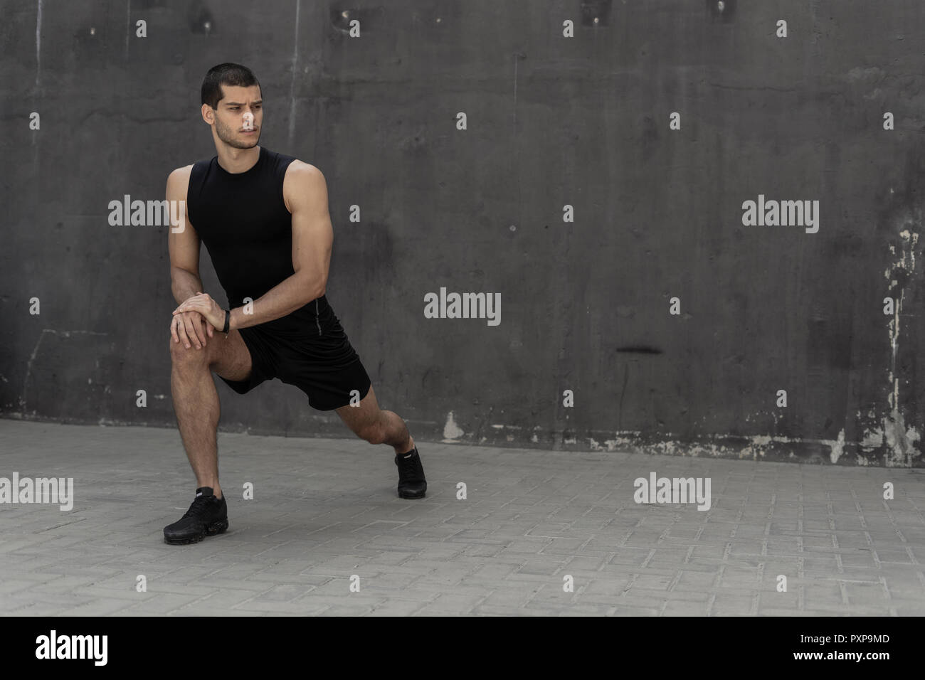 Bello e atletico uomo riscaldamento stretching prima della formazione, con pareti grigie in background. Uno stile di vita sano e sportswear pubblicità. Foto Stock