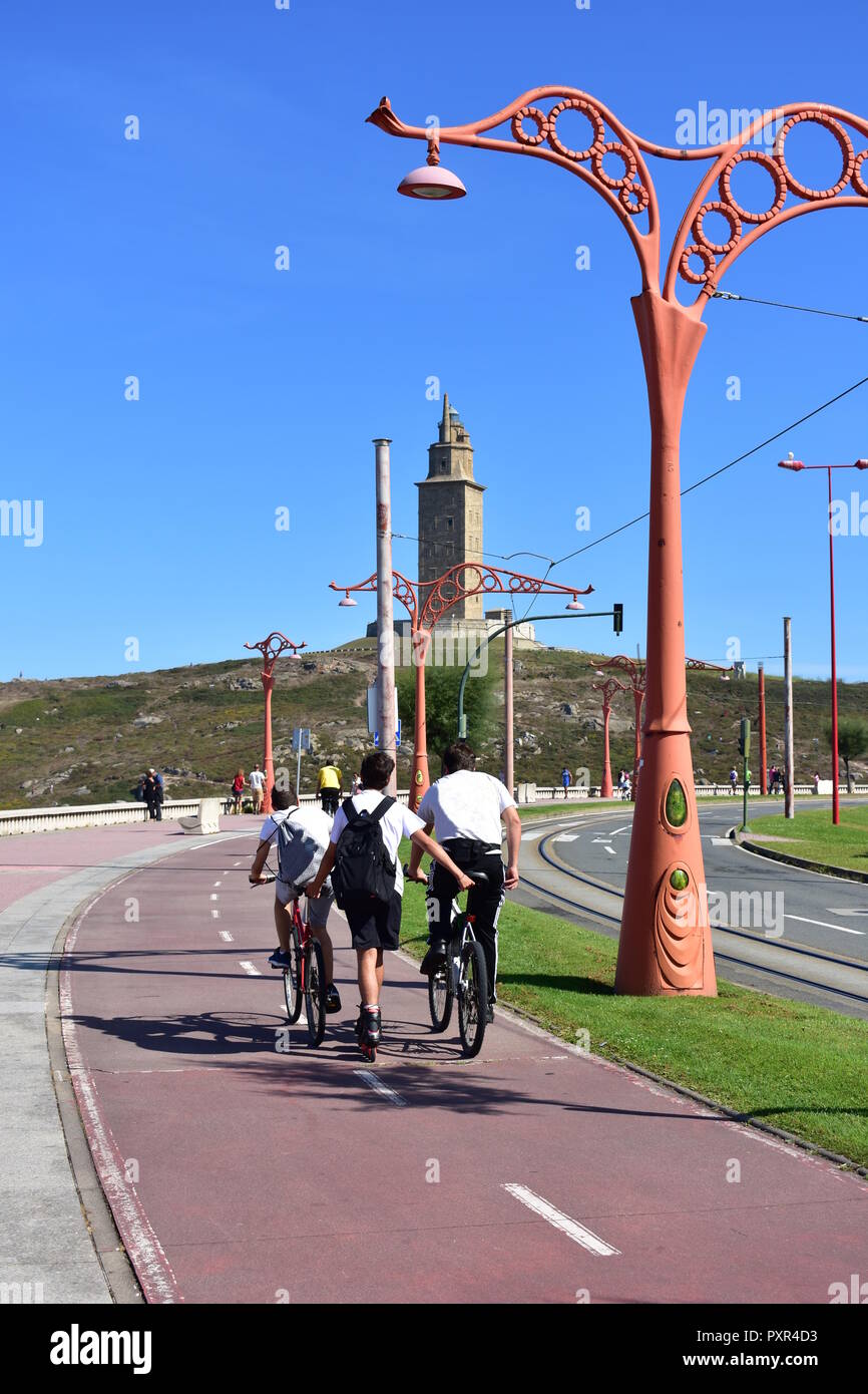 I giovani pattinano e pedalano in una passeggiata con sentieri e monumenti. Torre de Hercules parco, A Coruña, Galizia, Spagna. Foto Stock