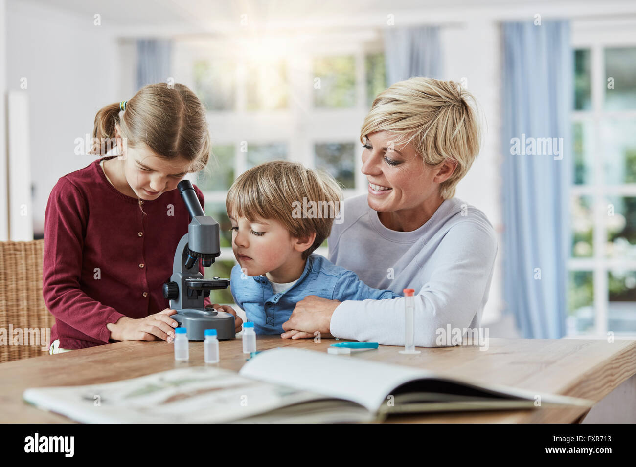 La madre con la figlia e il figlio mediante microscopio a casa Foto Stock