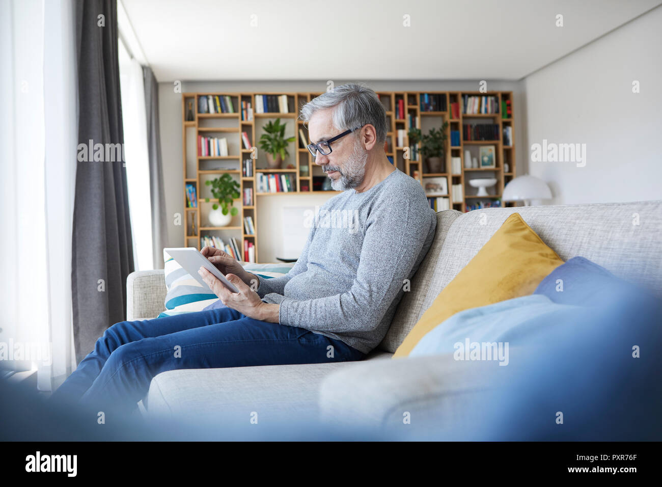 Uomo maturo seduto sul lettino al suo salotto utilizzando tablet Foto Stock