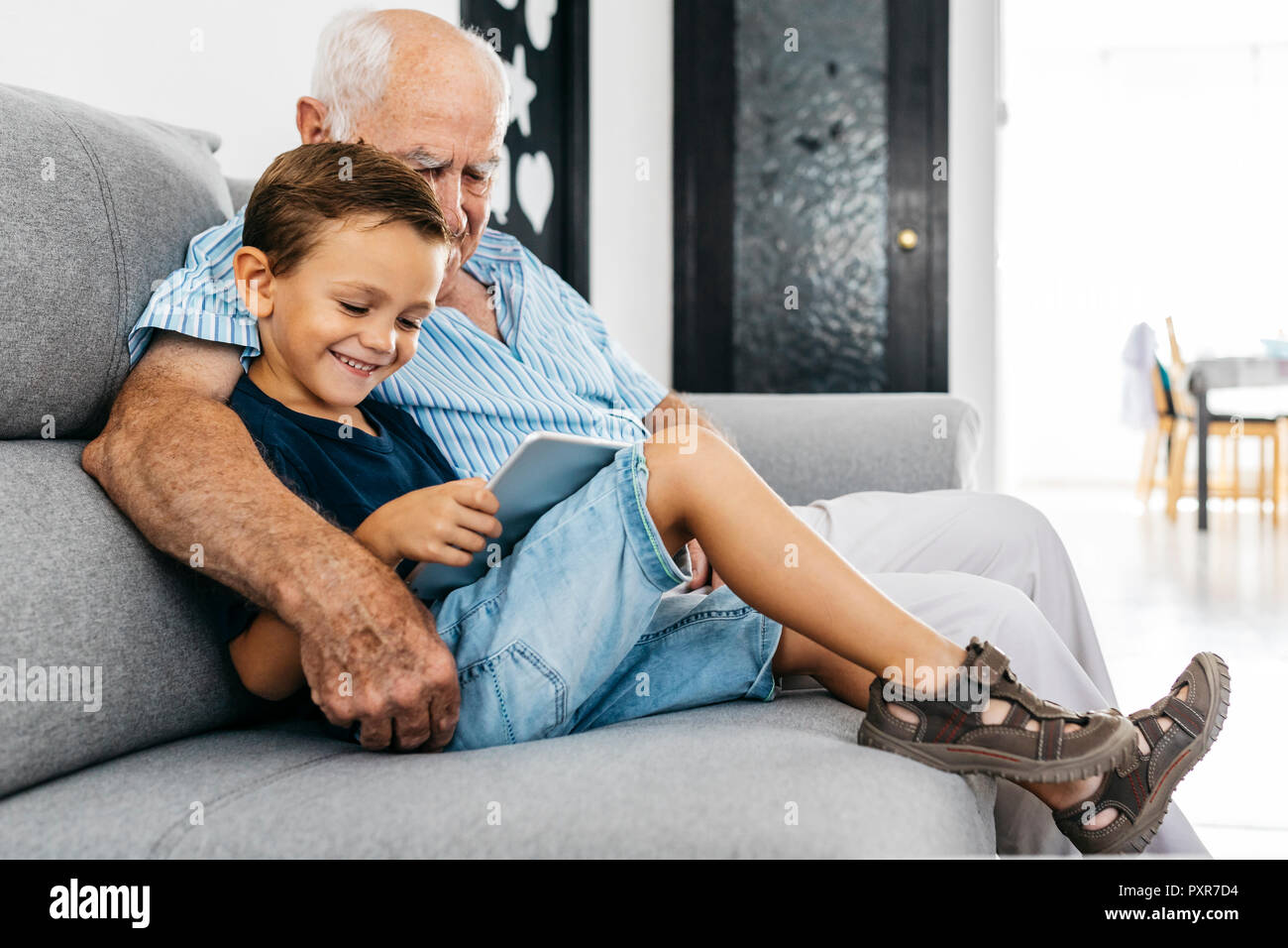 Nonno e nipote insieme seduti sul divano di casa guardando a tavoletta digitale Foto Stock